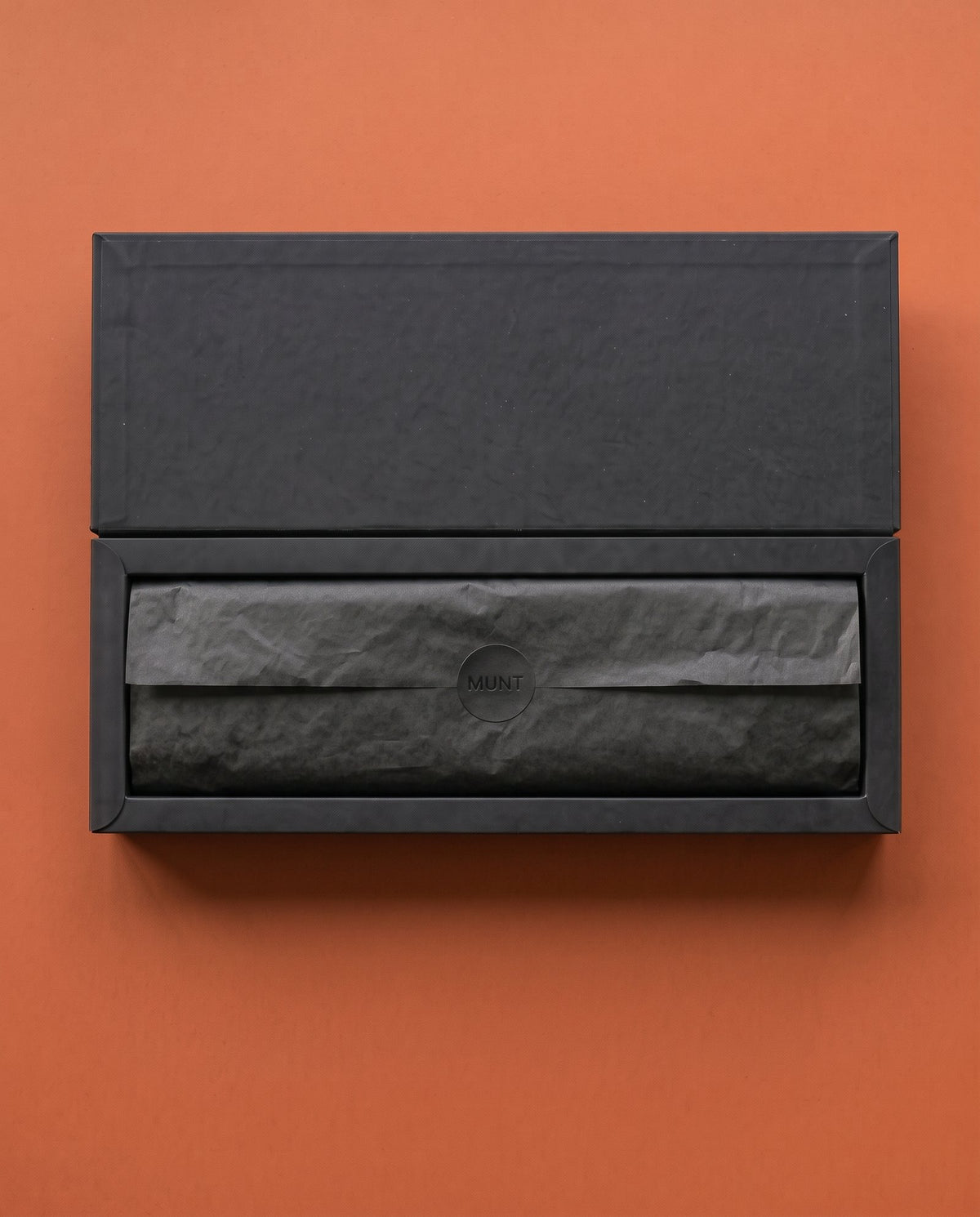 Lid open, the week wrapped in black tissue with the MUNT seal.